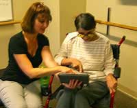 Barb helps a clientusing a wheelchair to access a tablet.